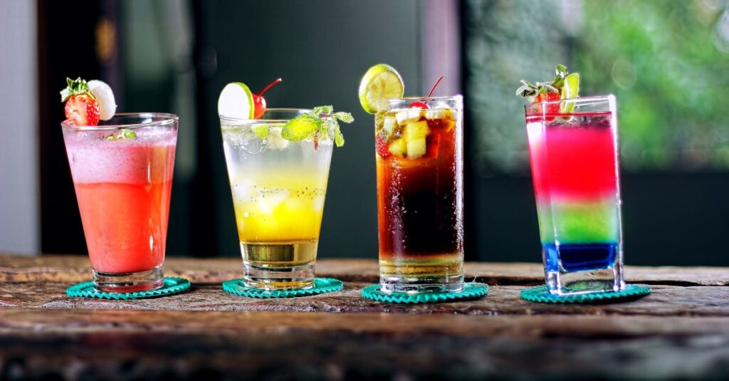 Colorful assortment of cocktails on a rustic wooden table, perfect for a refreshing summer evening.